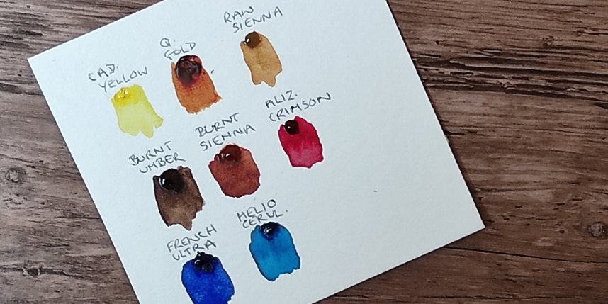 Dot card showing samples of watercolour paints lying on a desk top